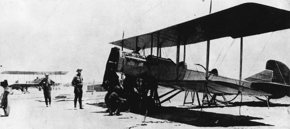 A Curtiss R-4LM with hood and propeller missing. The plane has there mechanics working on it while two supervisors look on. Another biplane is in the background.