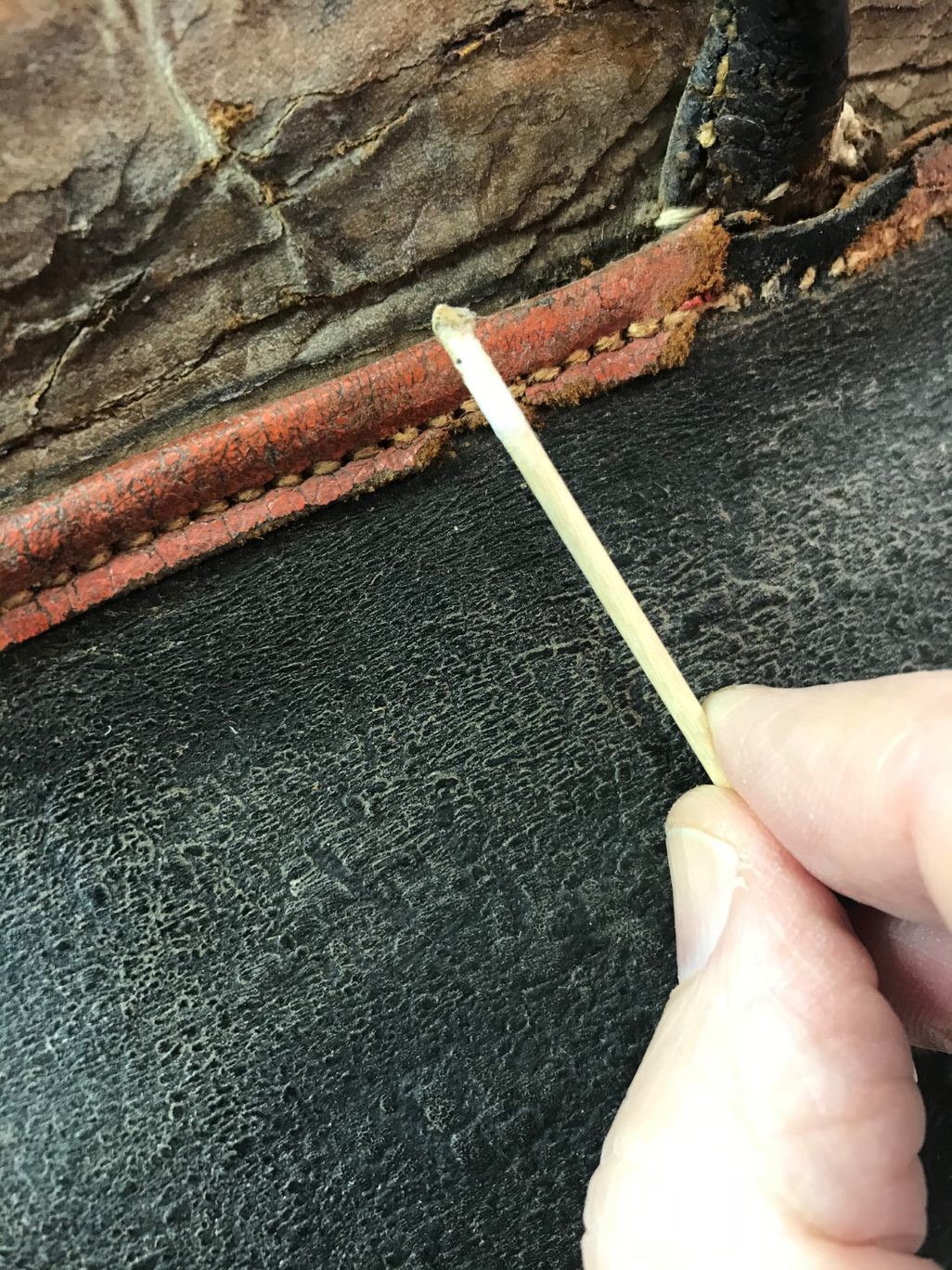 Close up photograph of hand holding small swab which is being used to clean the leather piping of the bag.