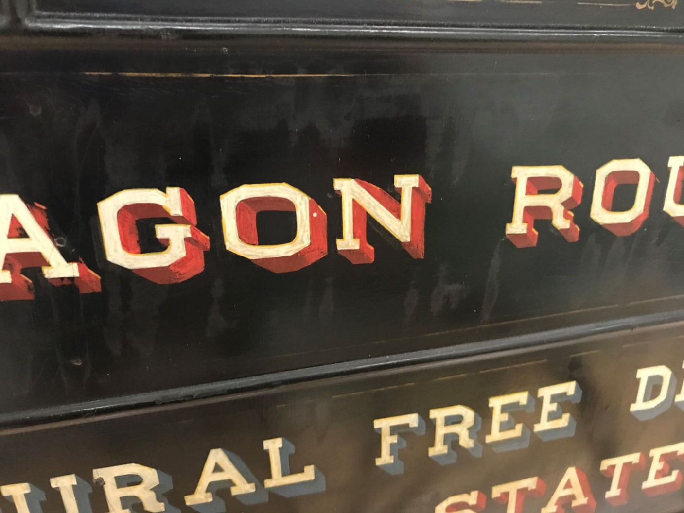 Close up color photograph of the side of a black model wagon. The black paint and red, yellow, and blue lettering is covered by a subtle white haze.