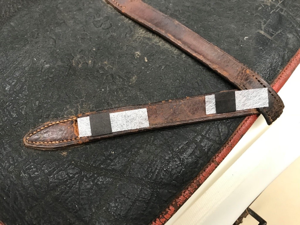 Photograph of worn letter strap held together with paper and polyester material. 