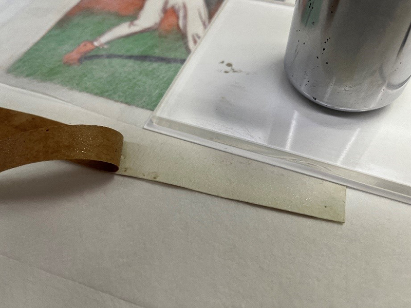 small metal weight on support board resting above a painting while tape is being removed