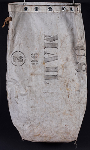 White canvas sack with metal grommets, leather cinch belt, and label holder; heavily soiled from use; marked U.S. MAIL