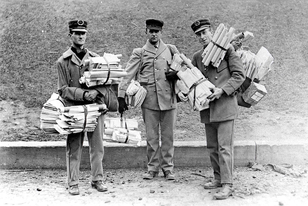 Three mail carriers holding many parcels and newspapers.