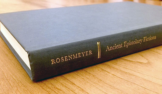 Blue-grey book laying on a wood table with spine facing out with the name 'Rosenmeyer' in gold, separated by two vertical gold bars, from the words 'Ancient Epistolary Fictions' in gold.