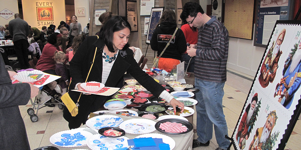 Visitors picking crafting supplies from a table laden with card decorations.