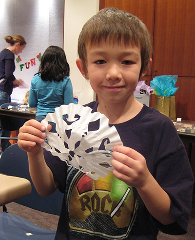 A young visitor facing the viewer and holding a paper snowflake.