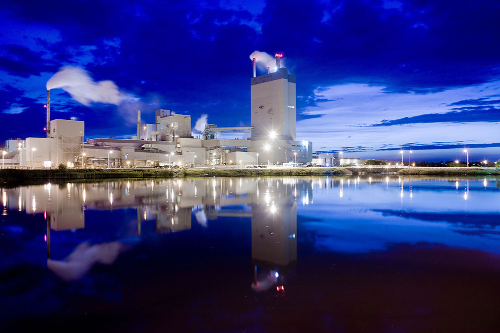 The Domtar Mill at nighttime with lights reflecting off a small lake in the foreground