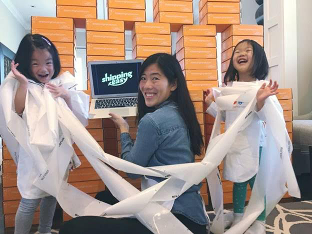 A woman and two little girls using the ShippingEasy application on a computer and planing playing with paper.