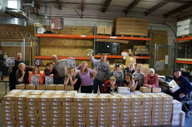 Employees posing behind stacks of boxes in a warehouse.