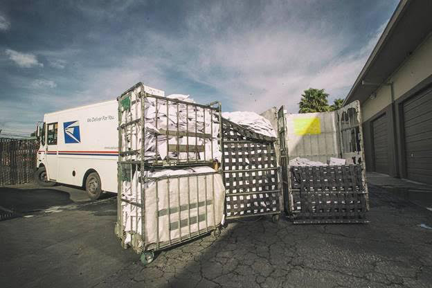 Carts full of mail being loaded into a Postal Service truck.