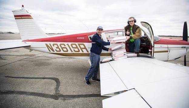 Employee unloading boxes from a small airplane handing them to a mail carrier.