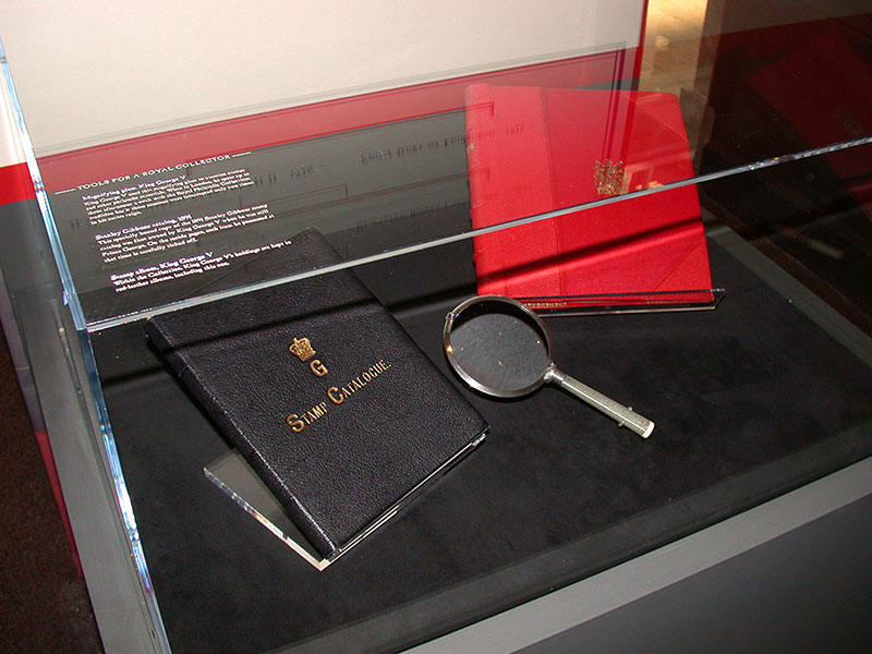 Exhibit case containing a stamp catalogue, a magnifying glass, and a stamp album.