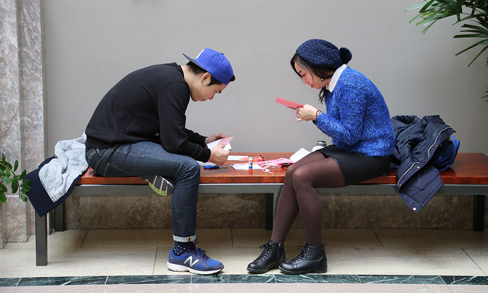 Two young adults sitting on a bench and working on Valentine’s Day cards.